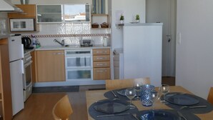 A compact kitchen with modern appliances, a dining area with a wooden table and chairs, and a small refrigerator.