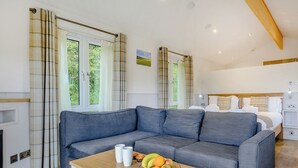 Une chambre moderne avec un canapé gris, une table basse en bois sur laquelle sont disposés des fruits, et un lit doté d’une tête de lit.