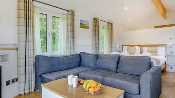 A modern room with a grey sofa, a wooden coffee table with fruit, and a bed with a headboard.