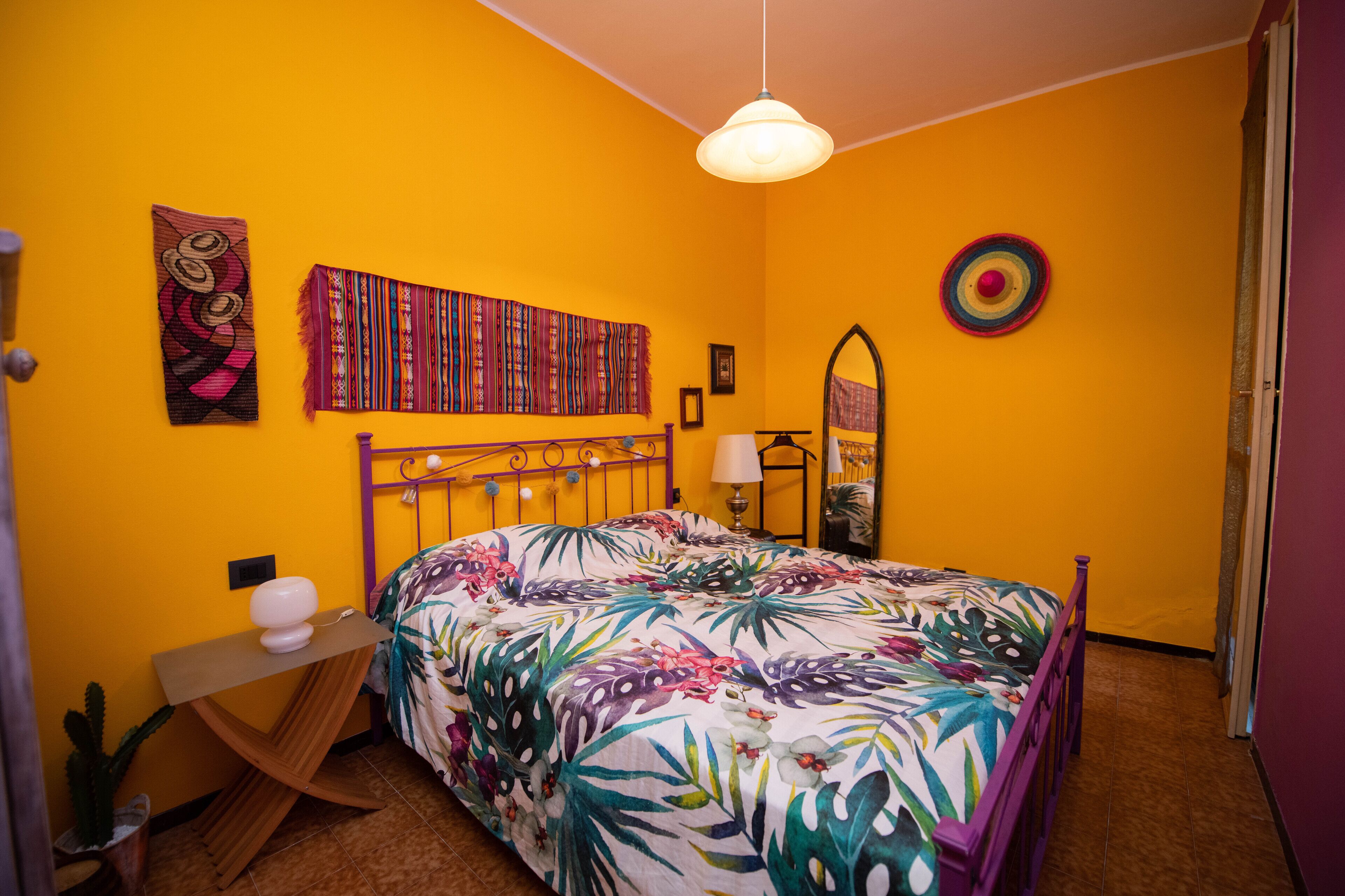 A bedroom with a bed, a bedside table, a lamp, a mirror, and wall decorations.
