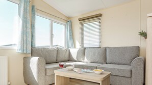 Un salon d’angle avec un canapé gris, une table basse en bois et une fenêtre équipée de stores.