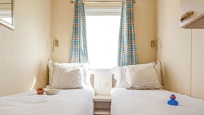 Une chambre d’hôtel avec deux lits, une fenêtre avec des rideaux, une petite table avec un muffin et un canard en plastique.