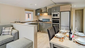 A compact kitchen with modern appliances, a dining area with a table set for two, and a sofa in the adjacent living area.