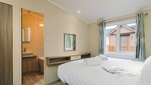 A hotel room with a bed, a bathroom, a window with curtains, and a view of a wooden building outside.