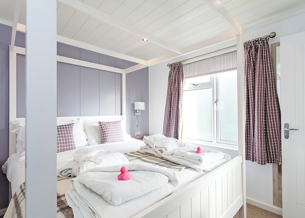 A bedroom with a bed, pillows, a bedside table, a lamp, a window with curtains, and a door. - 4 bedroom accommodation in Wootton Bridge, Nr Cowes (Wootton Bridge, Nr Cowes)