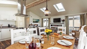 Une cuisine spacieuse équipée d’appareils électroménagers modernes, un coin repas avec une table en bois mise pour le repas, et un salon avec un téléviseur et des sièges confortables.