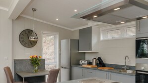 A modern kitchen with a dining area, a clock, and a vase with flowers. - This charming one-bedroom lodge boasts all the home comforts you need. (Cheddar)