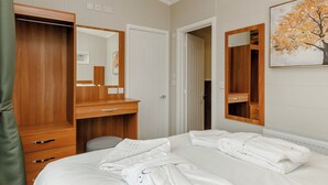 A hotel room with a bed, a wooden wardrobe, a mirror, and a painting on the wall. - This charming one-bedroom lodge boasts all the home comforts you need. (Cheddar)