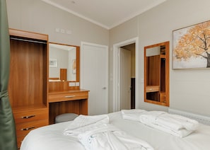 Hotellihuone, jossa on sänky, puinen vaatekaappi, peili ja taulu seinällä.