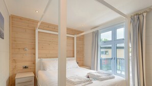 A four-poster bed with a wooden headboard, a bedside table with drawers, and a window with curtains.