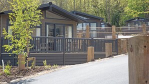 A modern cabin with a deck, surrounded by trees and a fence.