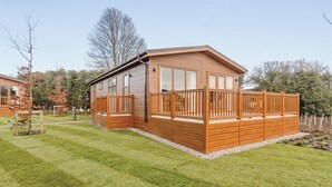 A wooden cabin with a deck, surrounded by a well-maintained lawn and trees. - 2 bedroom accommodation in Canterbury (Canterbury)