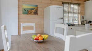 Ett rum med träpanel på väggarna, ett matbord, stolar, en fruktskål, ett kylskåp och ett fönster med persienner.