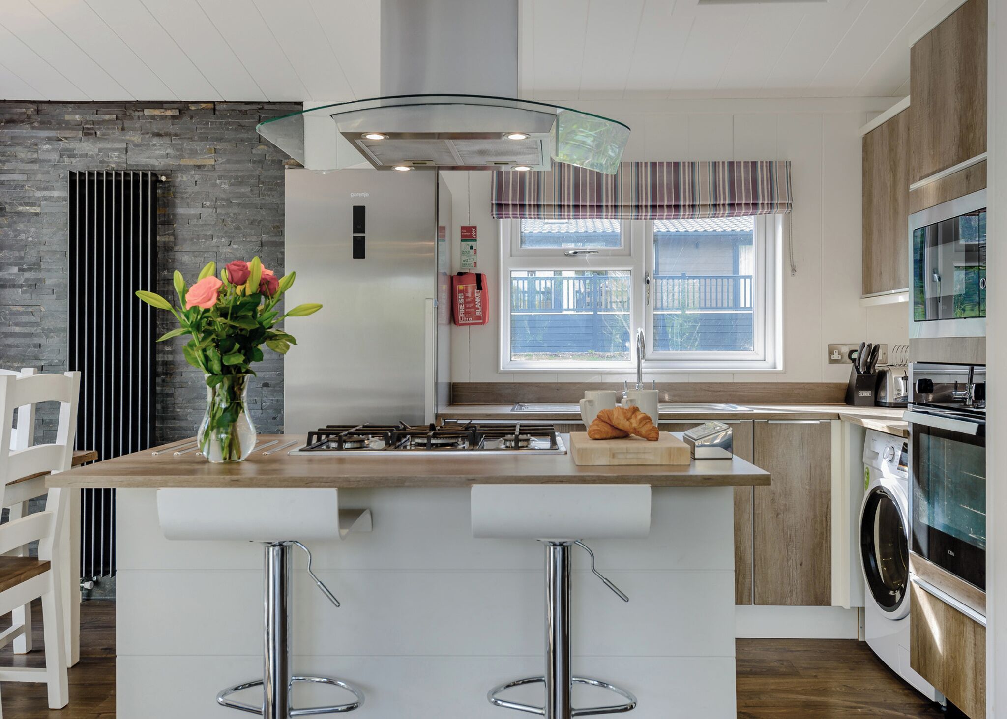 A modern kitchen with a central island, bar stools, a gas stove, a microwave, and a built-in oven.