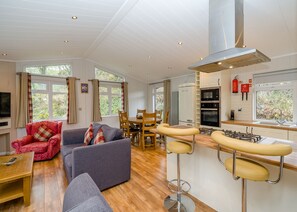 A modern kitchen with a gas stove, oven, and a stainless steel range hood. There is a dining area with a table and chairs, and a living room with a sofa and armchairs. - 2 bedroom accommodation in Bewaldeth, Keswick (Bewaldeth, Keswick)