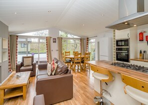 A modern kitchen with a gas stove, double oven, and a dining area with a sofa and wooden chairs. - Uvedale Premier Select (Bewaldeth, Keswick)