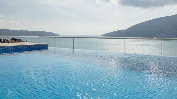 A clear blue pool with a glass barrier, surrounded by mountains and a clear sky. - Hotel Krušo (Herceg Novi)