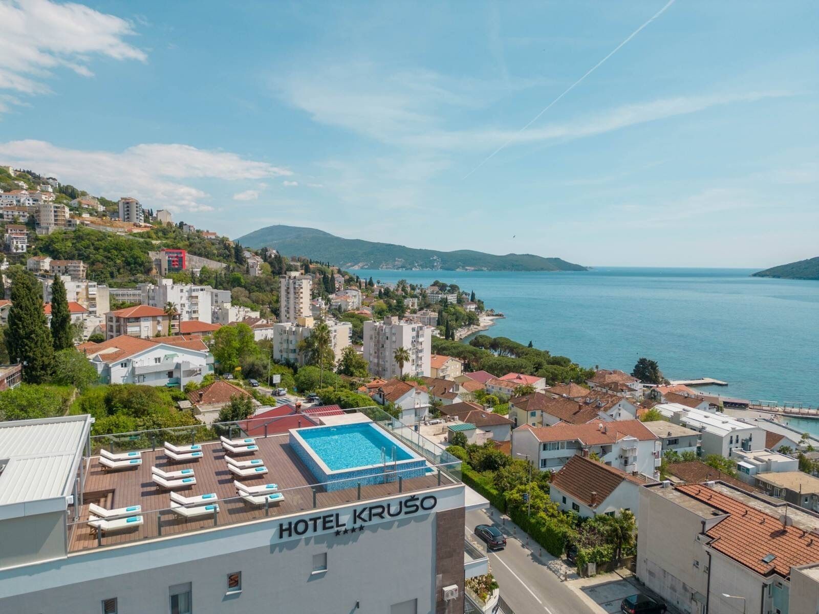 A hotel named HOTEL KRUSO with a rooftop pool area, surrounded by residential buildings and a view of the sea.