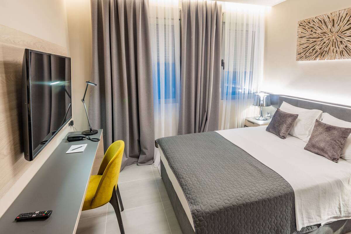 A hotel room with a bed, a desk with a TV, a chair, and curtains.