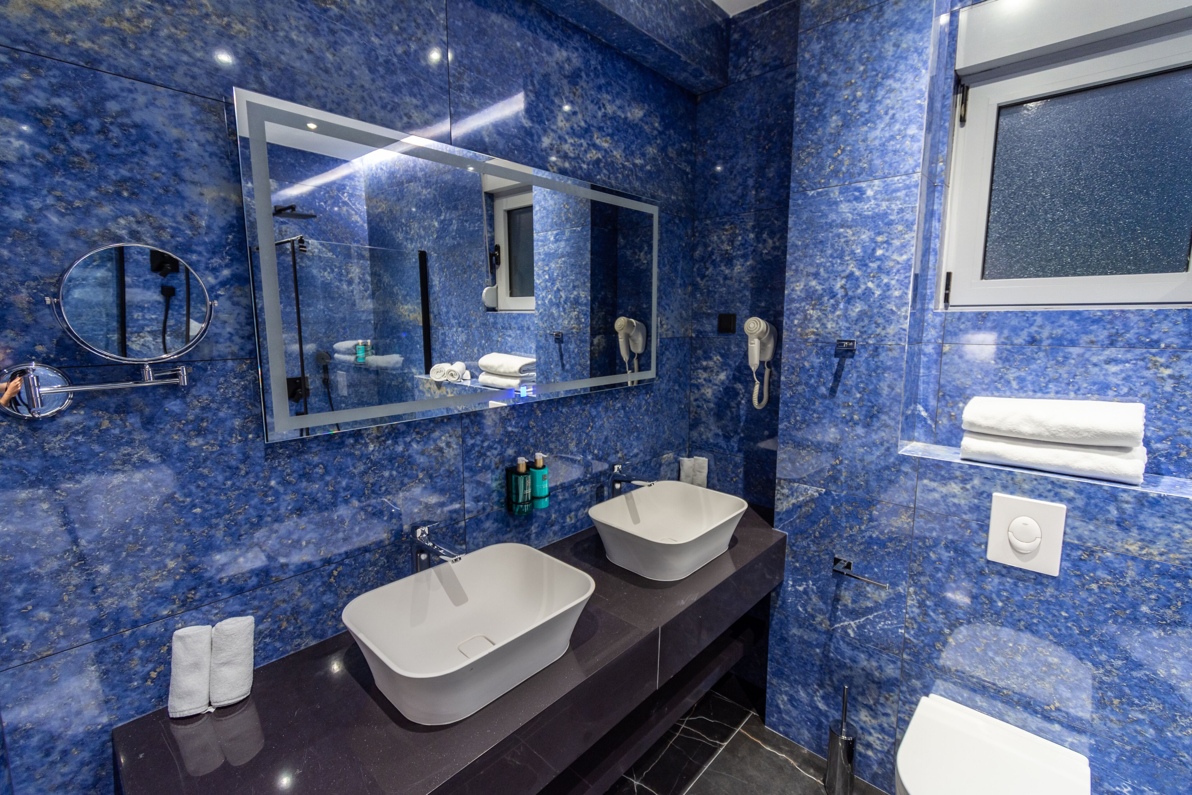A modern bathroom with two sinks, a large mirror, and a toilet.