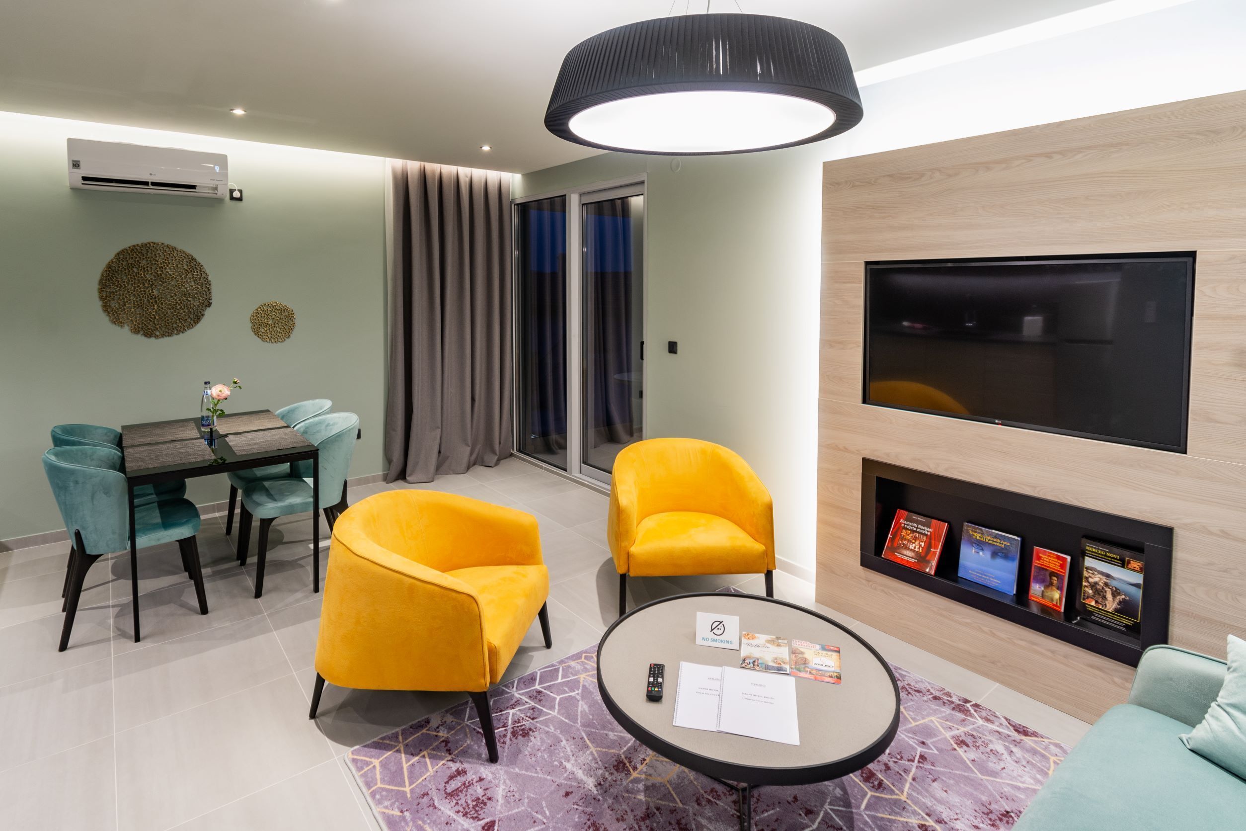 A modern living room with a dining area, a flat-screen TV, and a bookshelf.