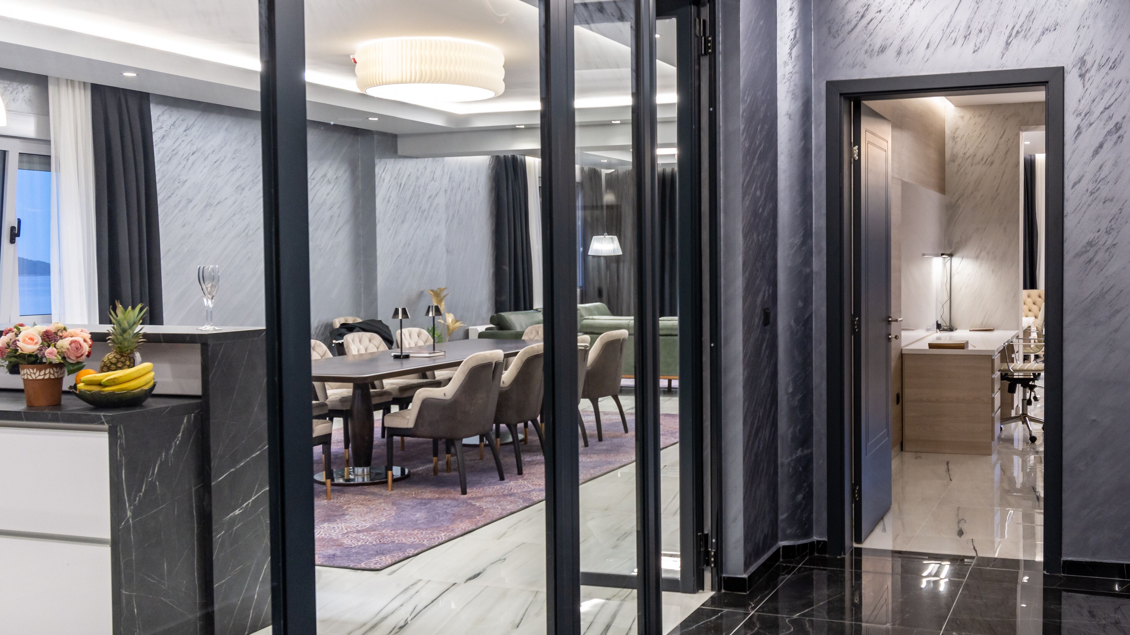 A modern hotel room with a marble floor, a dining area with a table and chairs, and a separate workspace with a desk and chair.