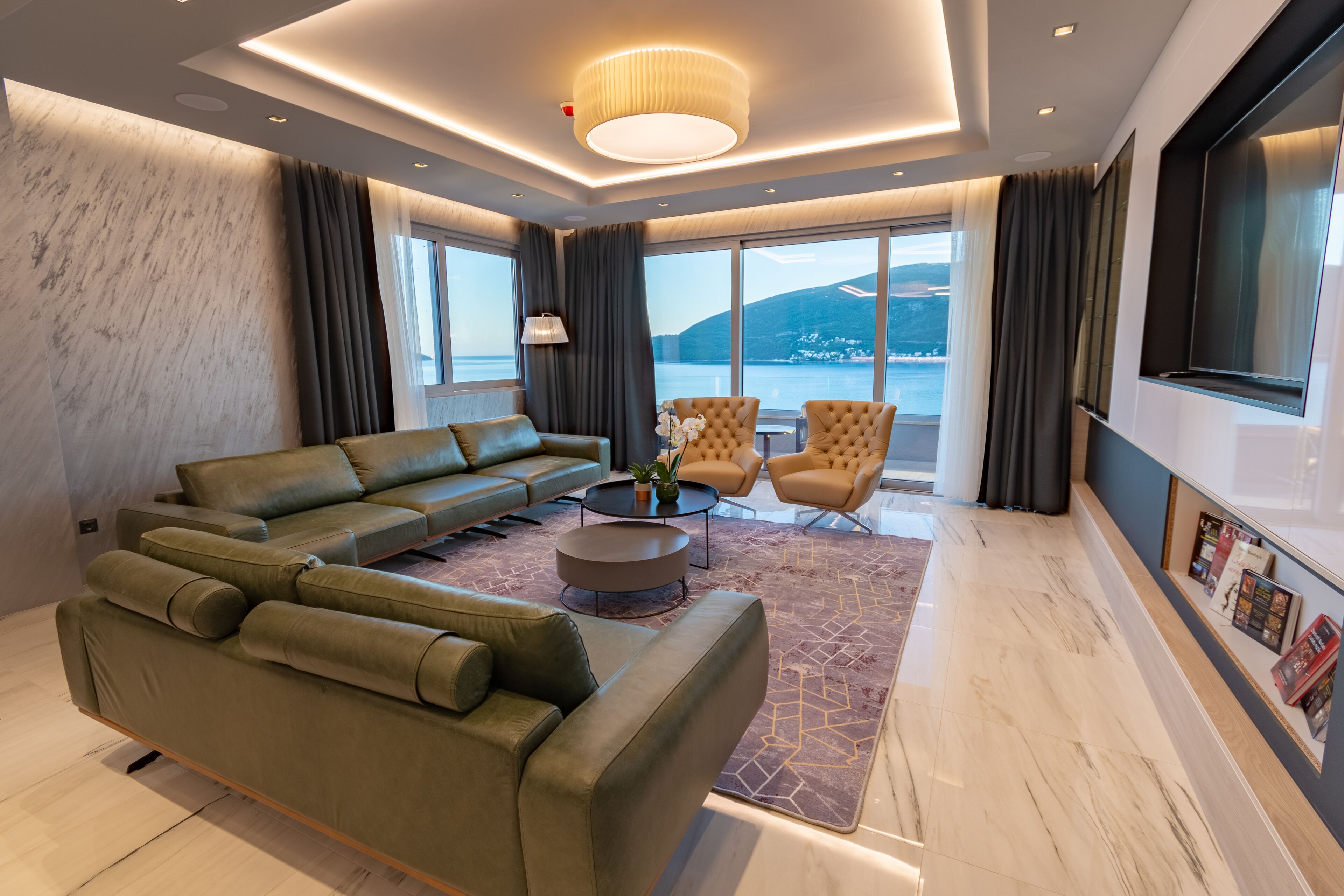 A modern living room with a sectional sofa, a round coffee table, and a view of the sea.