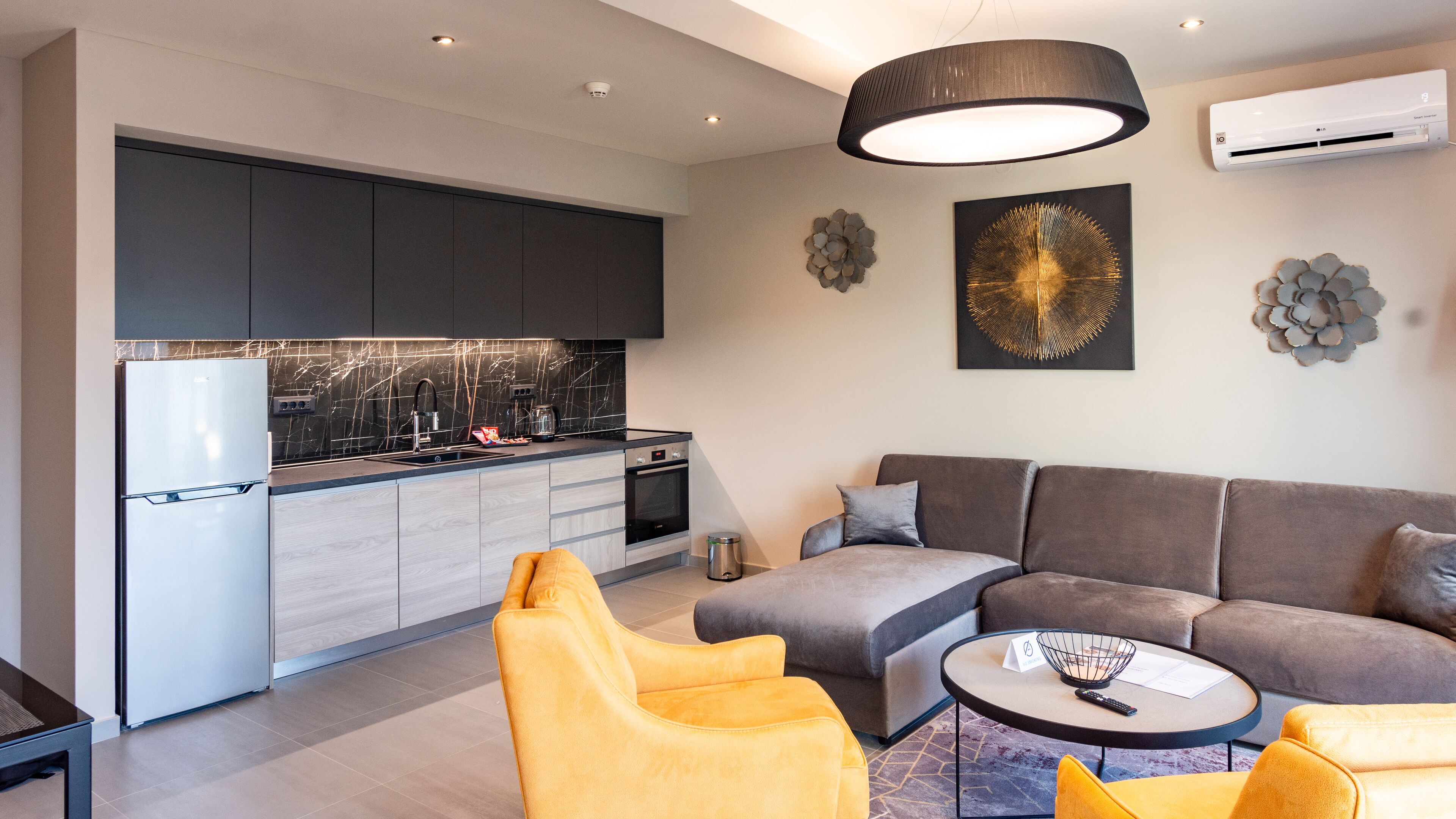 A modern kitchen with a built-in oven and a refrigerator, a grey sofa set, and a yellow armchair.