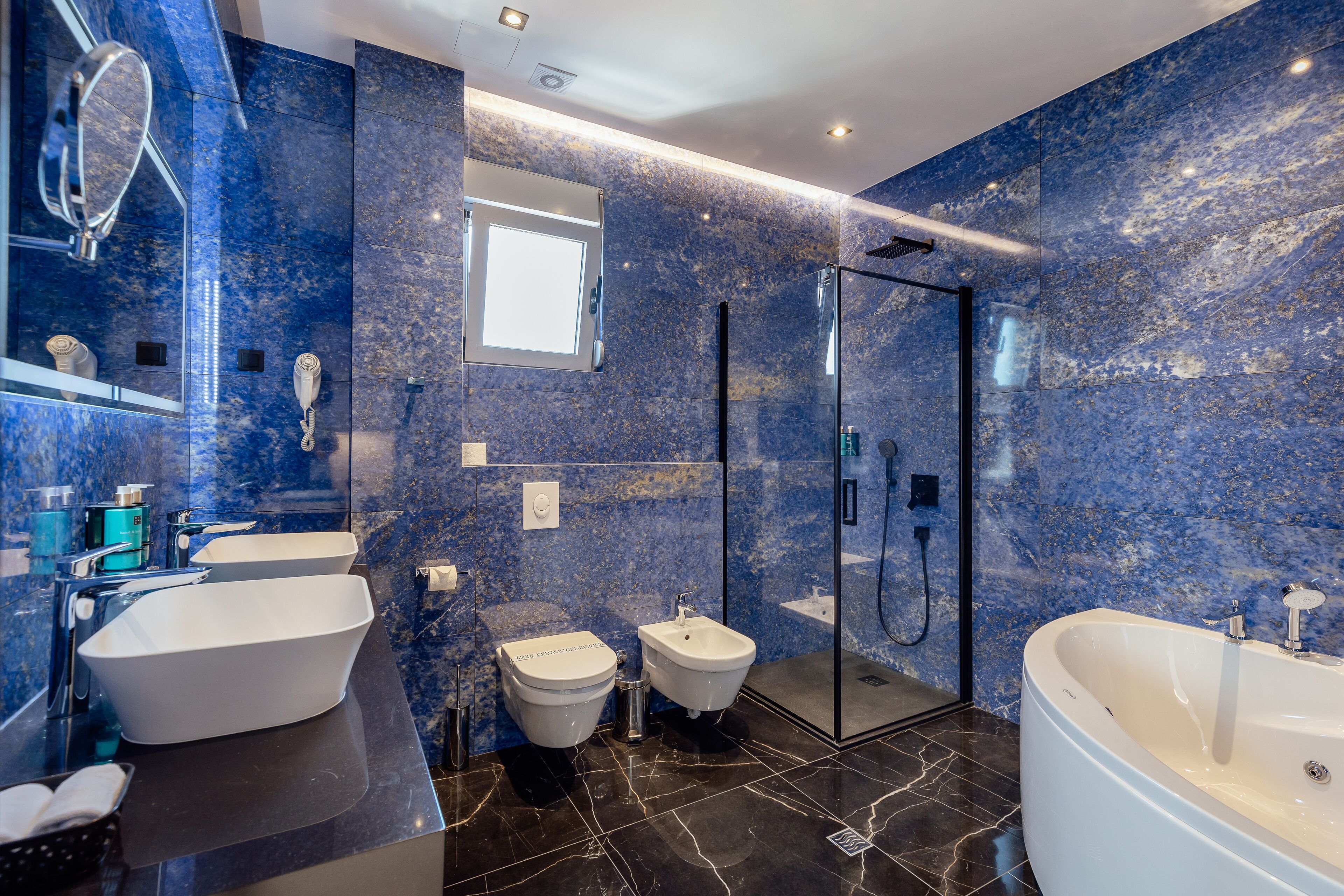 A modern bathroom with a large bathtub, two sinks, a bidet, and a glass-enclosed shower.