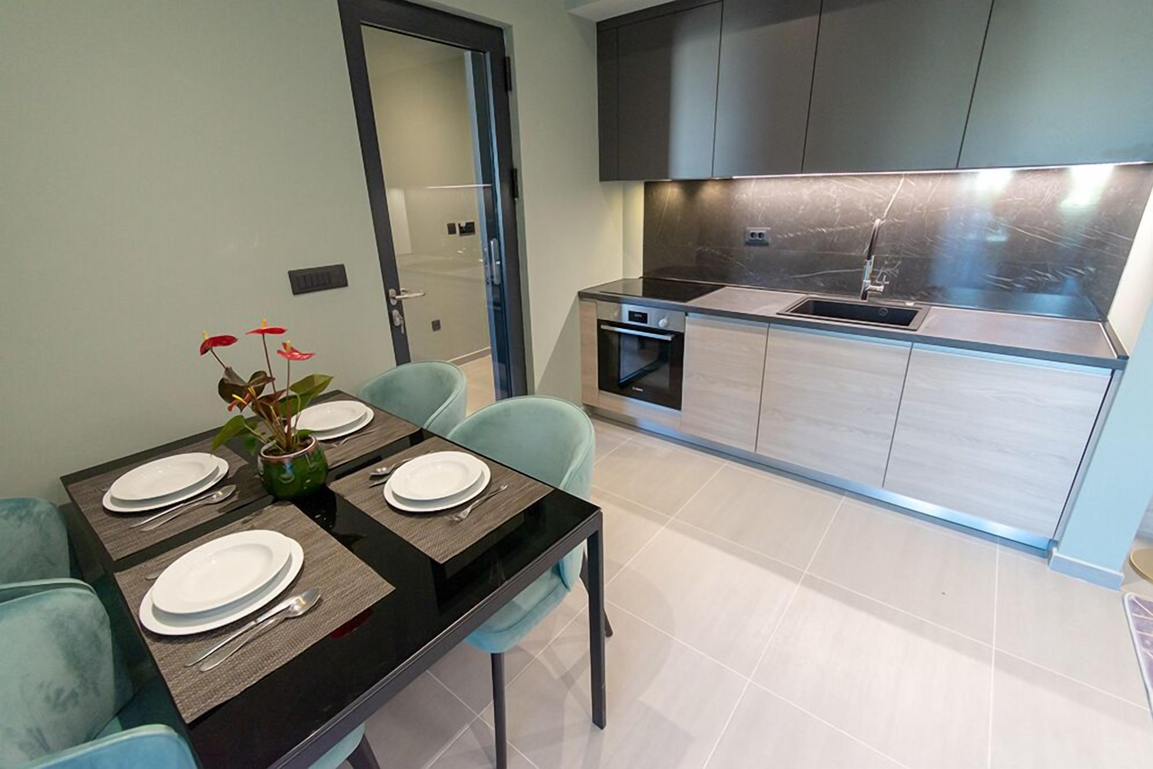Una cucina moderna con zona pranzo. Si vede un tavolo apparecchiato per quattro persone, un piccolo forno e un lavello.