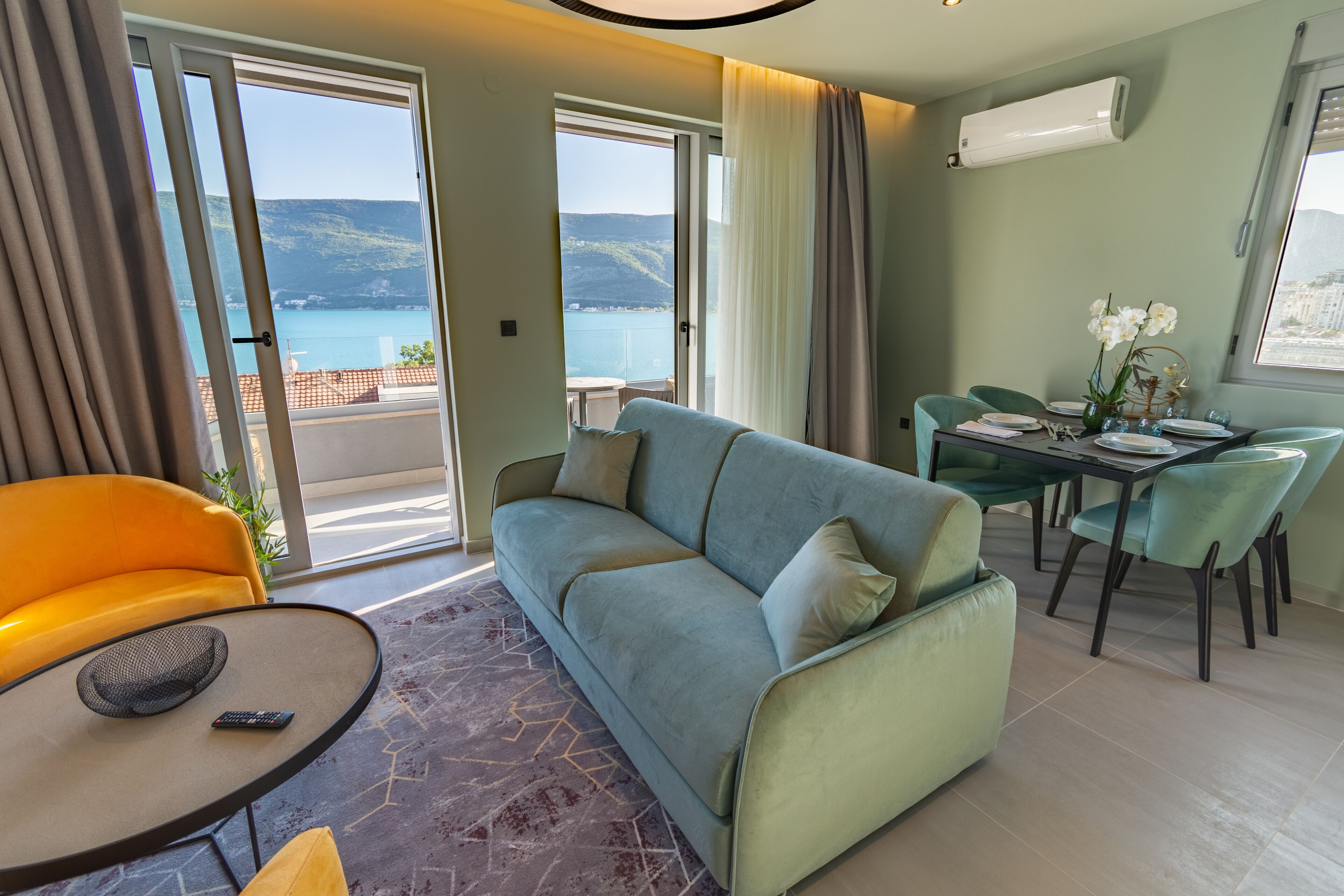 A modern living room with a sofa, a dining table with chairs, and a view of the sea.