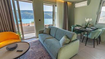 A modern living room with a sofa, a dining table with chairs, and a view of the sea.