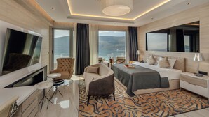 A modern hotel room with a large bed, a TV, a desk, and a view of the mountains. - Hotel Krušo (Herceg Novi)