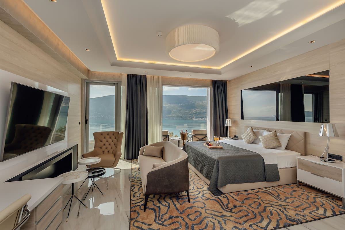 A modern hotel room with a large bed, a TV, a desk, and a view of the mountains.