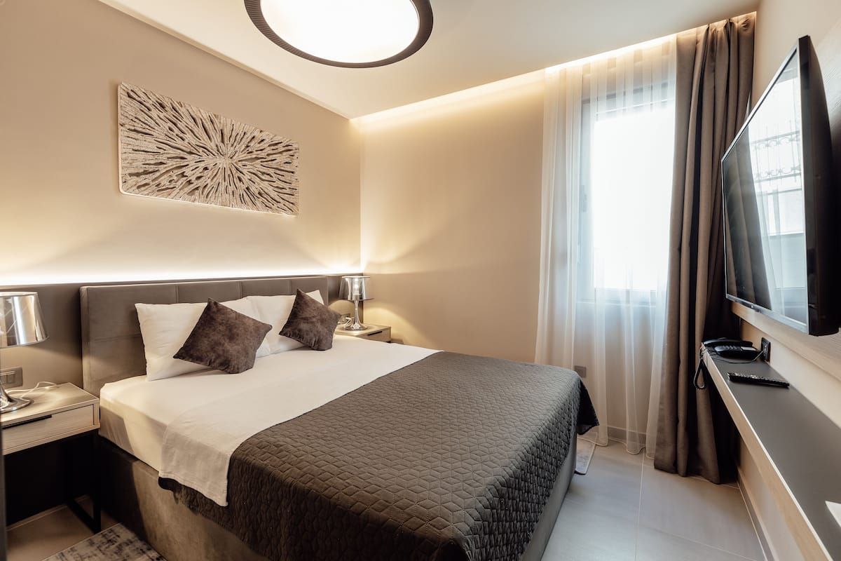 A hotel room with a bed, bedside tables, a TV, and a window with curtains.