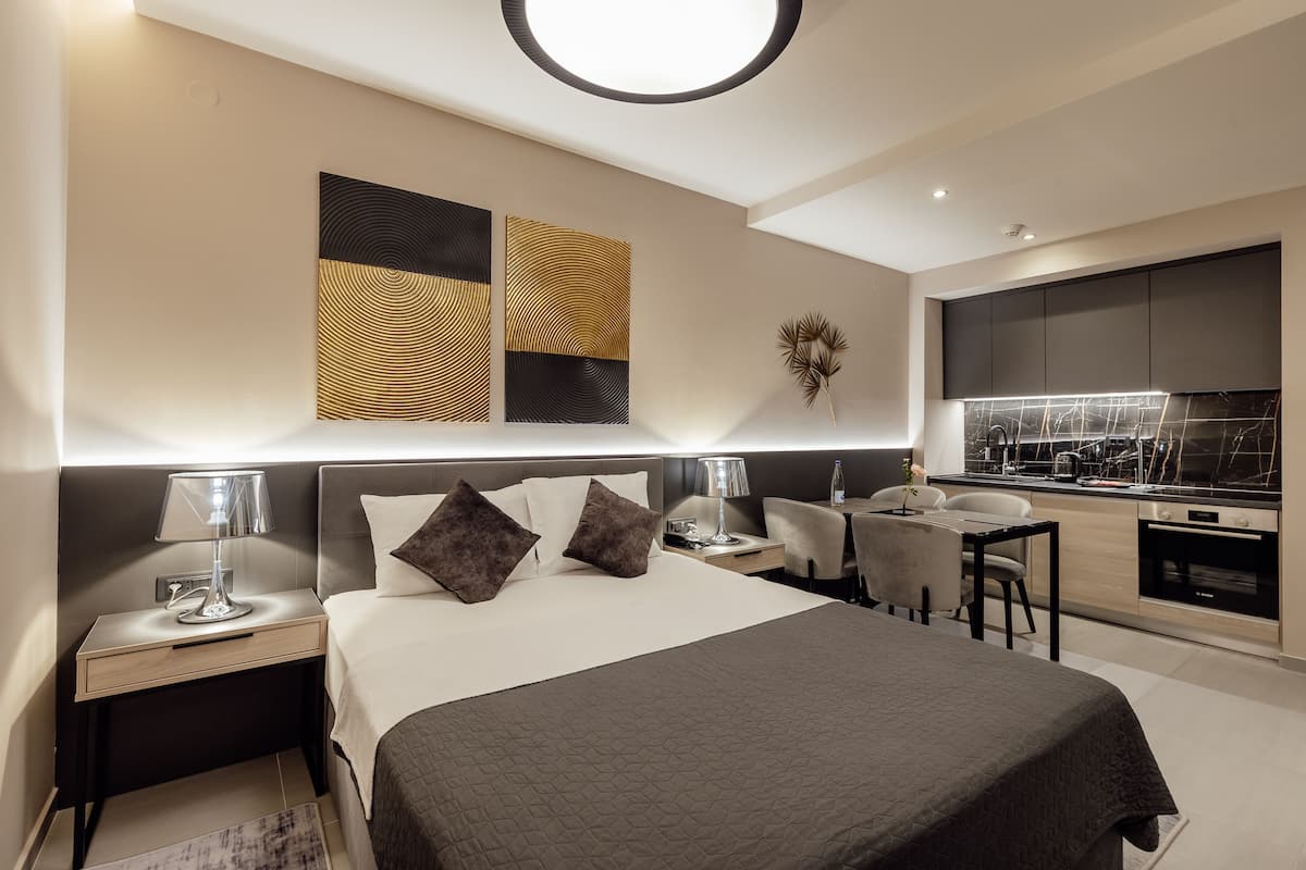 A modern hotel room with a large bed, bedside tables, a desk, and a kitchenette.