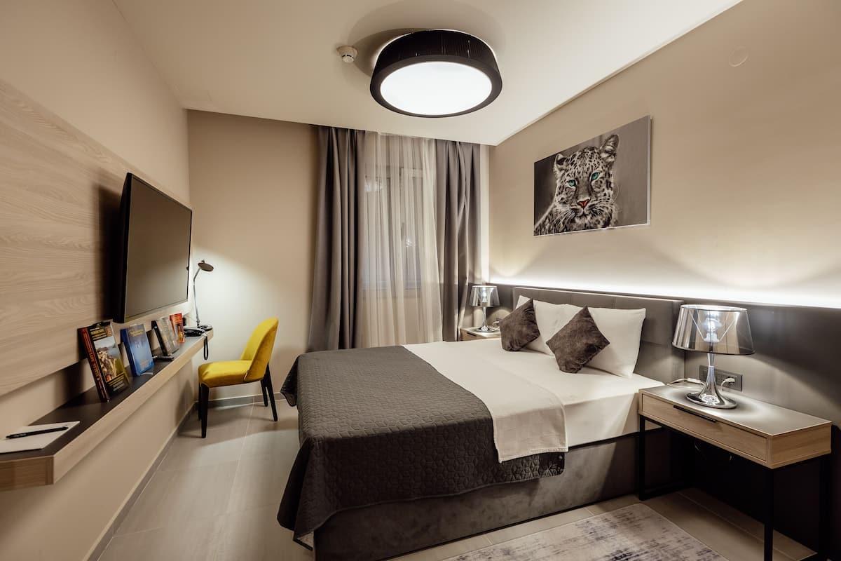 A modern hotel room with a bed, bedside table, lamp, and a mounted TV.