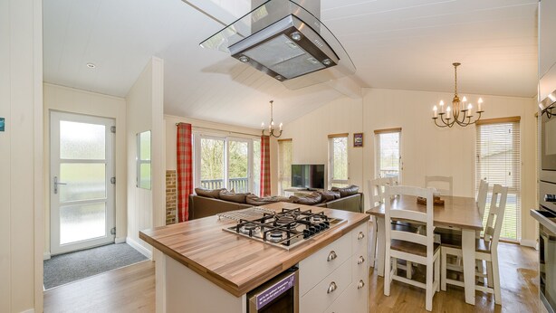 Een moderne keuken met een centraal eiland, houten vloer en een eethoek met witte stoelen.