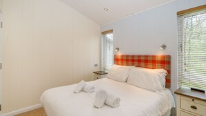 Een slaapkamer met een bed, een nachtkastje, een lamp en een raam met jaloezieën.