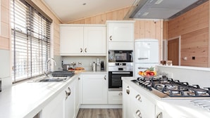Una cocina compacta con muebles blancos, horno empotrado, estufa a gas y ventana con persianas.