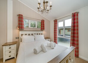 Une chambre à coucher avec un grand lit, des tables de chevet, un lustre et une fenêtre avec des rideaux.