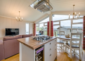 Una cocina moderna con una isla central, un comedor con sillas blancas, un sofá y un televisor.