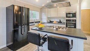 A modern kitchen with a central island, black appliances, and a stainless steel range hood.