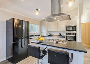 A modern kitchen with a central island, black appliances, and a stainless steel range hood.