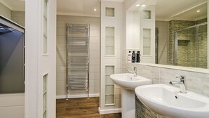A modern bathroom with a glass shower enclosure, two sinks, and a towel rack.