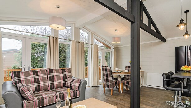 A modern living room with a sofa, dining table, and chairs, large windows, and a staircase.