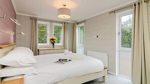 A bedroom with a bed, bedside tables, a window with curtains, a radiator, and a wall-mounted light fixture.
