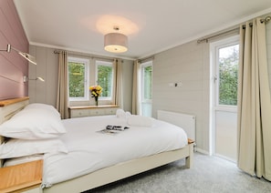 A bedroom with a bed, bedside tables, a window with curtains, a radiator, and a wall-mounted light fixture.