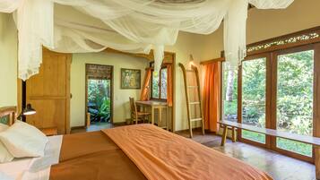 A bedroom with a bed, a desk, and a view of greenery through large windows.