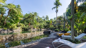 A wooden deck with lounge chairs and a small pool surrounded by tropical vegetation.